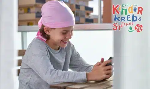 Ein krankes Kind mit Mütze spielt lachend