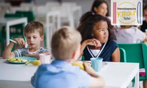 Kinder sitzen an einem Tisch und essen gemeinsam in einer Kantine