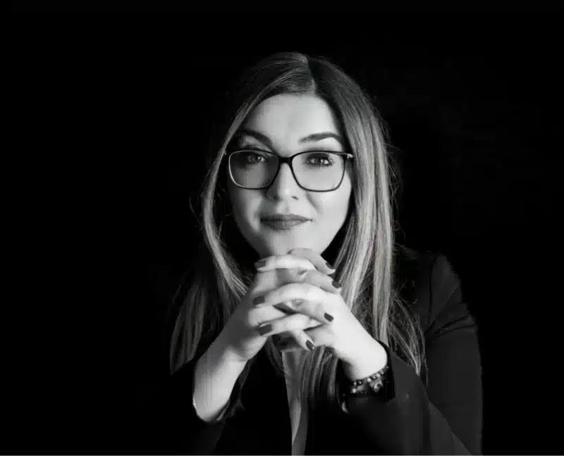 Sanja M. sitzt mit gefalteten Händen am Tisch